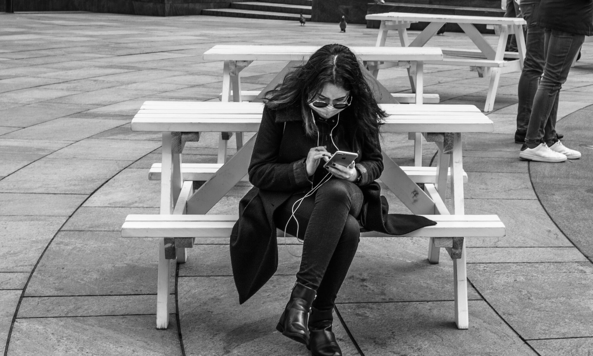 black and white photo of a woman on a bench using her smart phone